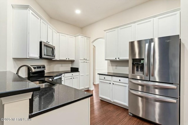 kitchen featuring kitchen peninsula, stainless steel appliances, dark wood-type flooring, white cabinetry, and dark stone counters