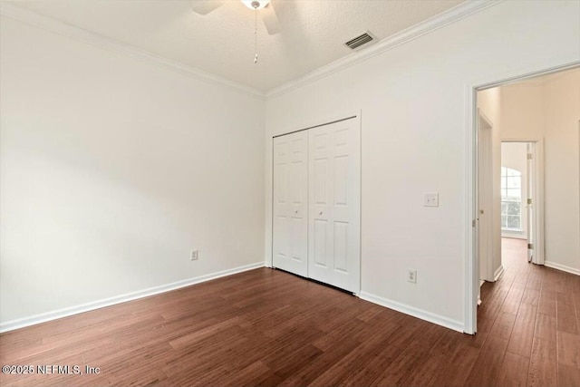 unfurnished bedroom with ceiling fan, dark wood-type flooring, ornamental molding, a textured ceiling, and a closet