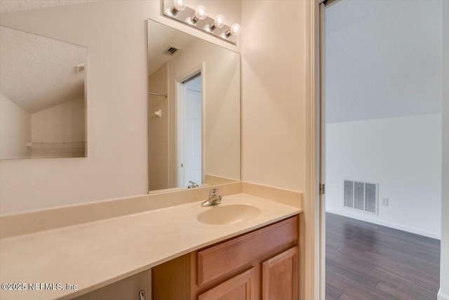 bathroom with wood-type flooring, a textured ceiling, vanity, and vaulted ceiling