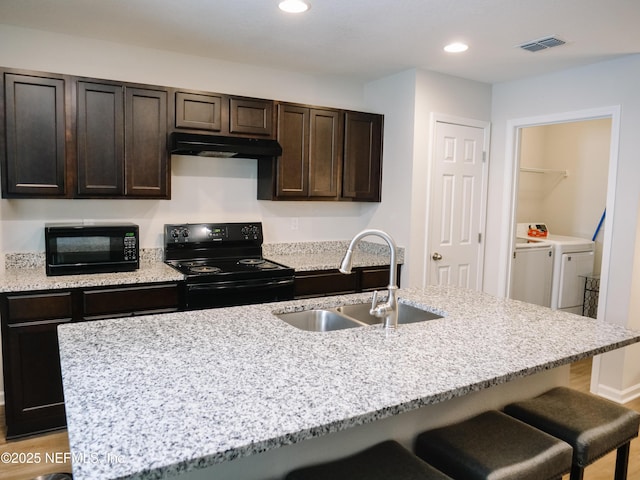 kitchen with dark brown cabinets, a kitchen island with sink, washing machine and dryer, black appliances, and sink