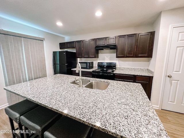 kitchen featuring black appliances, light stone counters, sink, and a kitchen bar