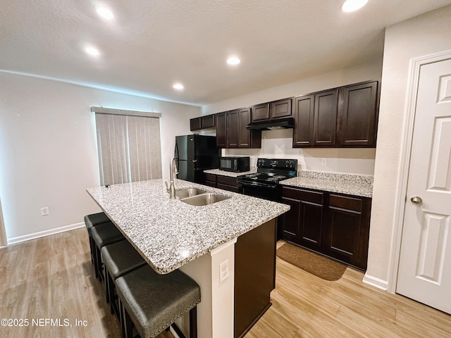 kitchen featuring sink, a breakfast bar area, black appliances, light hardwood / wood-style floors, and an island with sink