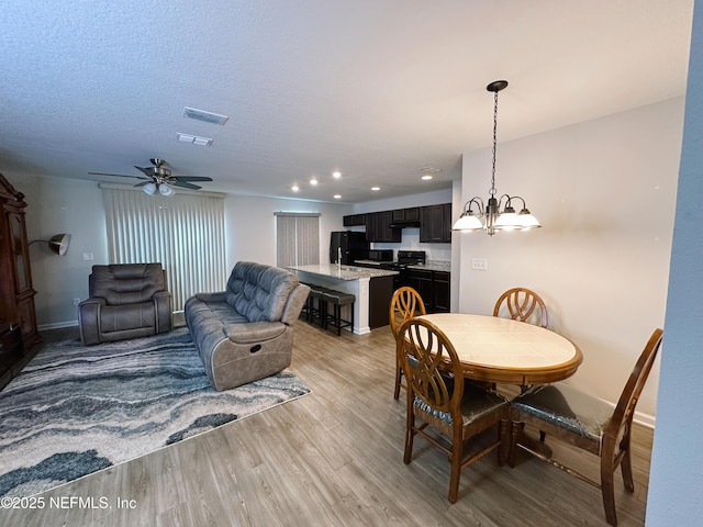 dining area with a textured ceiling, ceiling fan with notable chandelier, and light hardwood / wood-style floors