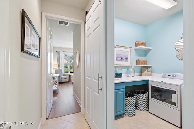 clothes washing area featuring light tile patterned floors, a barn door, laundry area, visible vents, and washer / clothes dryer