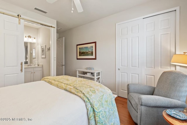 bedroom featuring a closet, visible vents, a barn door, connected bathroom, and wood finished floors