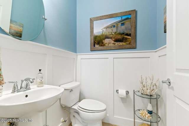 half bathroom with a wainscoted wall, a sink, and toilet