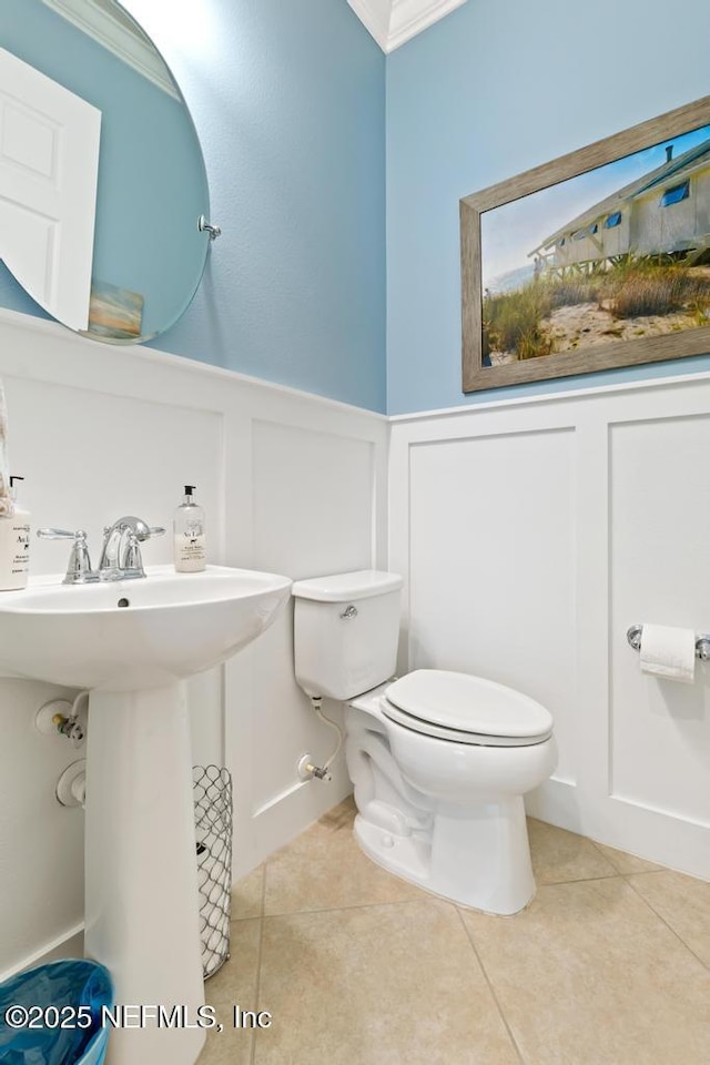 half bath featuring wainscoting, toilet, ornamental molding, tile patterned floors, and a decorative wall