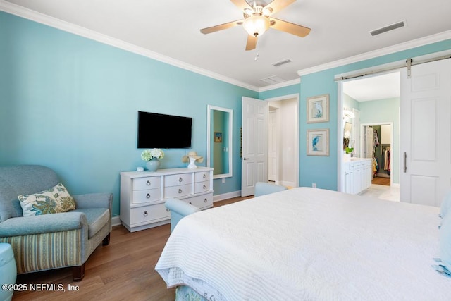 bedroom featuring light wood-style floors, visible vents, ornamental molding, and a barn door