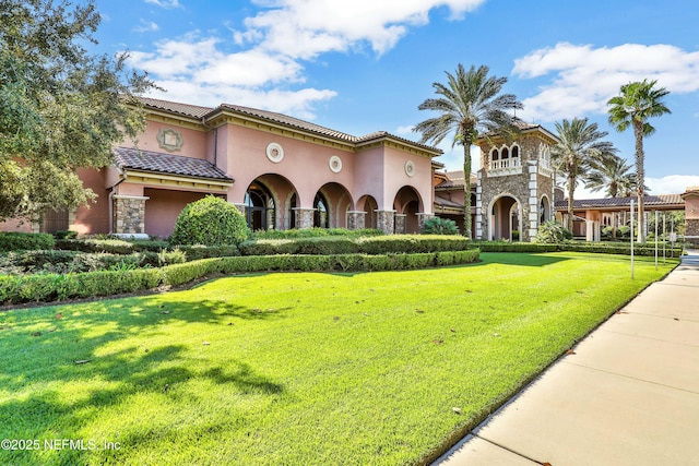 mediterranean / spanish house featuring stone siding, a tile roof, a front lawn, and stucco siding