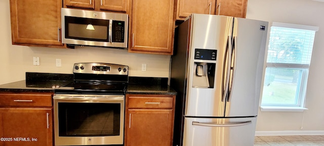 kitchen with brown cabinets, stainless steel appliances, and dark stone countertops