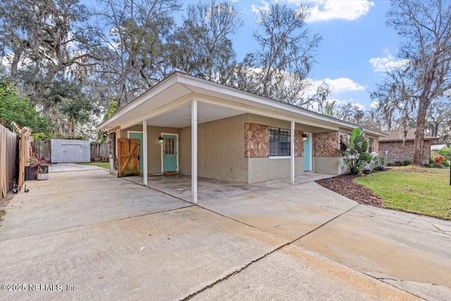 view of front of home with an outbuilding, concrete driveway, stucco siding, a carport, and a shed