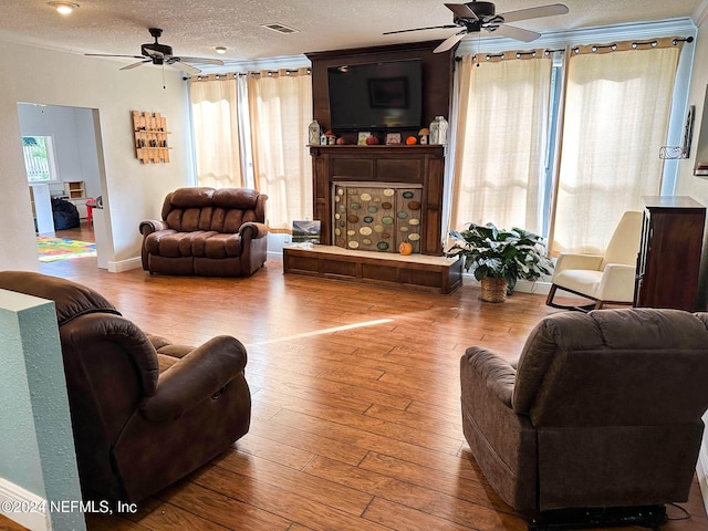 living room with light hardwood / wood-style flooring, a textured ceiling, ceiling fan, a fireplace, and ornamental molding