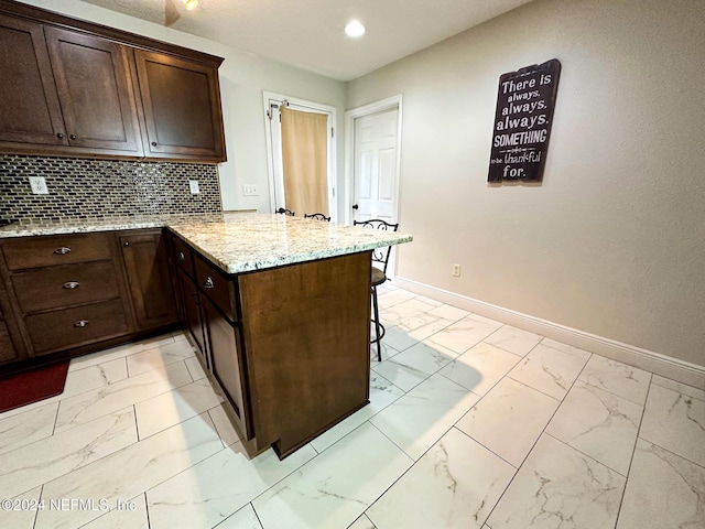 kitchen featuring tasteful backsplash, dark brown cabinets, a kitchen breakfast bar, light stone countertops, and kitchen peninsula