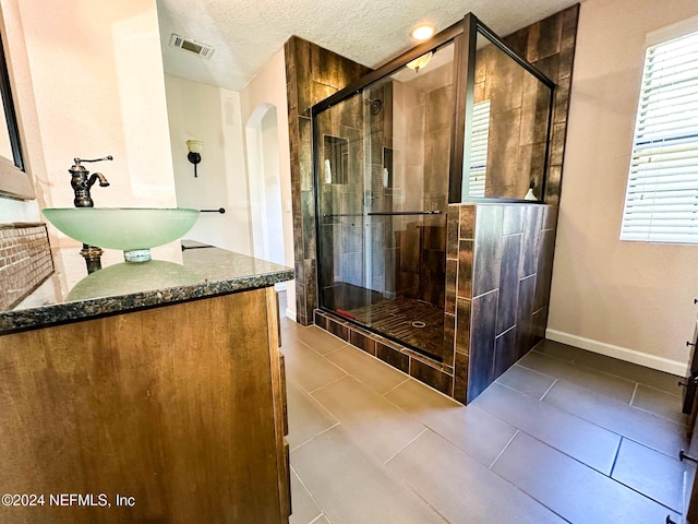 bathroom with a shower with shower door, vanity, a textured ceiling, and tile patterned floors