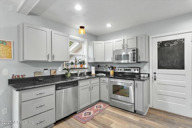 kitchen with sink, light wood-type flooring, gray cabinets, stainless steel appliances, and dark stone countertops