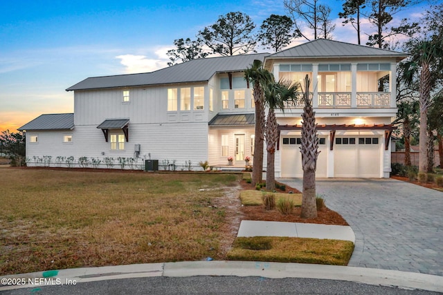 view of front facade with a lawn, metal roof, decorative driveway, a balcony, and an attached garage