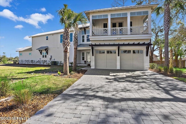 view of front of property featuring board and batten siding, a front yard, decorative driveway, a balcony, and an attached garage