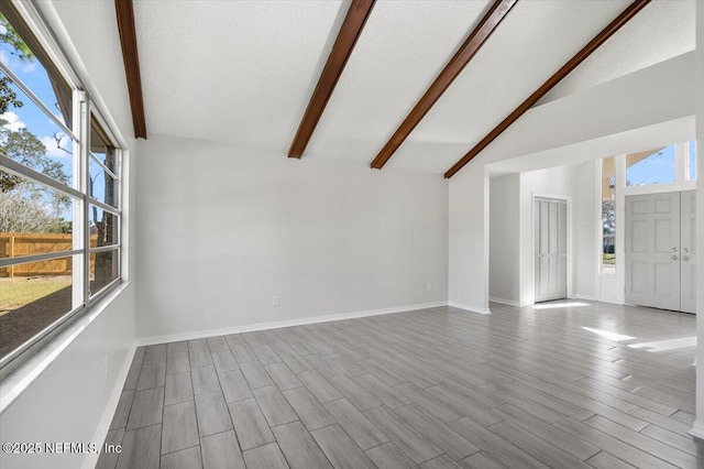 spare room with light wood-type flooring, vaulted ceiling with beams, and a textured ceiling