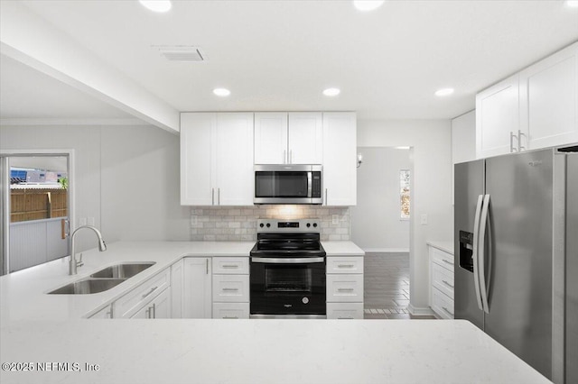 kitchen with appliances with stainless steel finishes, wood-type flooring, backsplash, sink, and white cabinetry