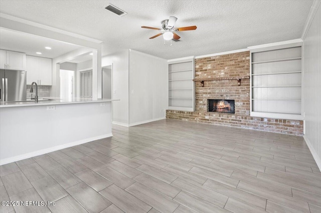 unfurnished living room featuring a fireplace, ceiling fan, built in shelves, and a textured ceiling