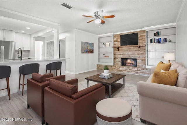 living room with a fireplace, ceiling fan, crown molding, and built in shelves