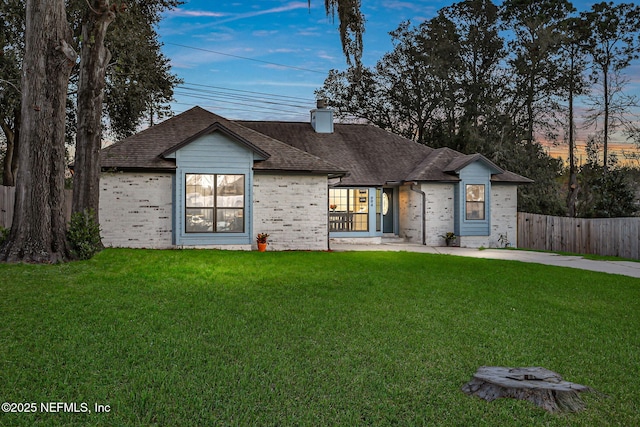 ranch-style house with brick siding, fence, roof with shingles, a lawn, and a chimney