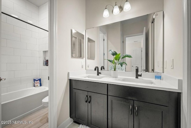 bathroom featuring toilet, double vanity, a sink, and wood finished floors