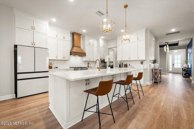 kitchen featuring visible vents, backsplash, freestanding refrigerator, light wood-type flooring, and premium range hood