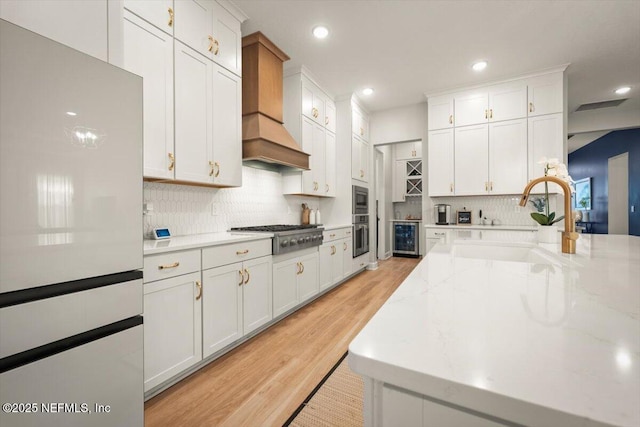 kitchen with white cabinets, wine cooler, custom range hood, and stainless steel appliances