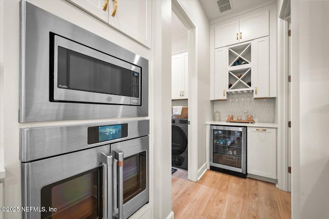 bar with wine cooler, appliances with stainless steel finishes, backsplash, a bar, and washer / dryer