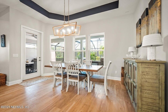 dining space with light wood-type flooring, a raised ceiling, and baseboards