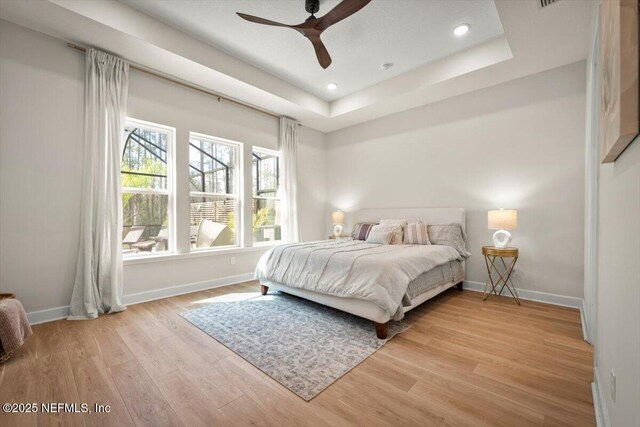 bedroom featuring a raised ceiling, light wood-style flooring, and baseboards