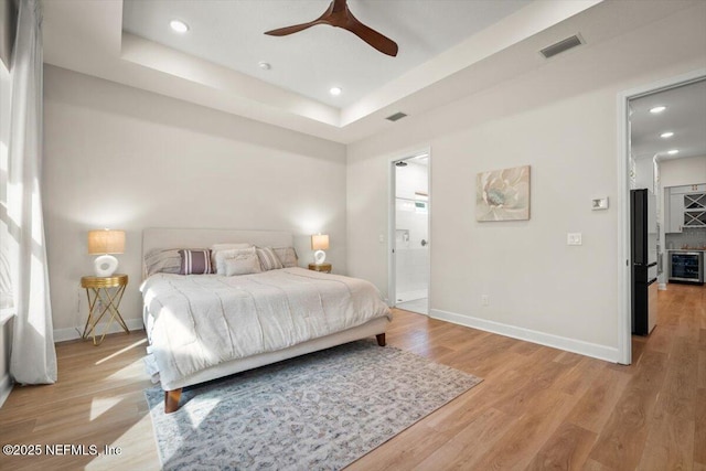 bedroom with light wood-type flooring, beverage cooler, visible vents, and a tray ceiling