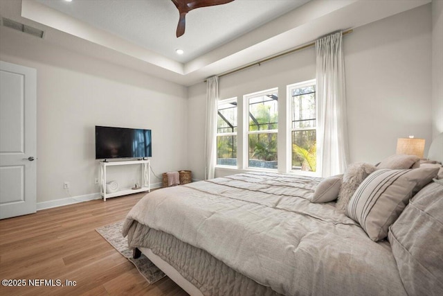 bedroom featuring recessed lighting, wood finished floors, visible vents, baseboards, and a tray ceiling