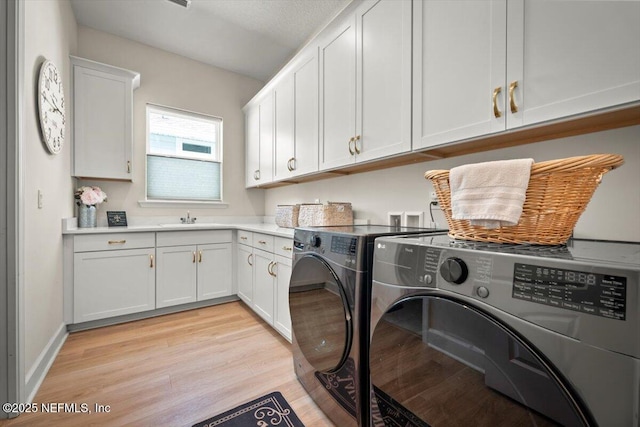 clothes washing area featuring cabinet space, washing machine and dryer, a sink, light wood-type flooring, and baseboards