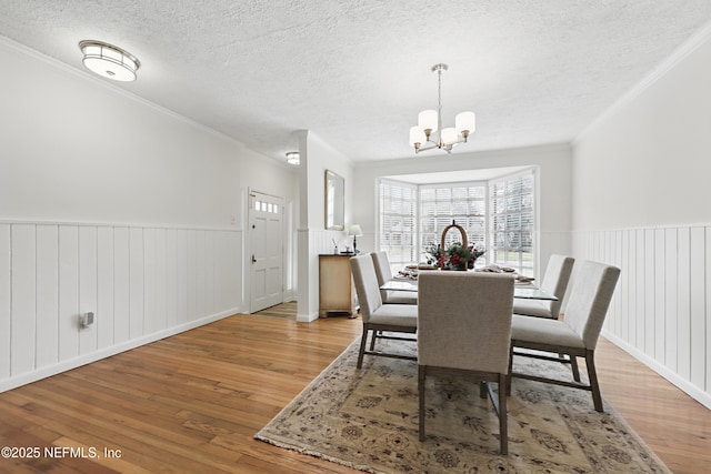 dining area featuring a wainscoted wall, ornamental molding, a textured ceiling, light wood-style floors, and a chandelier