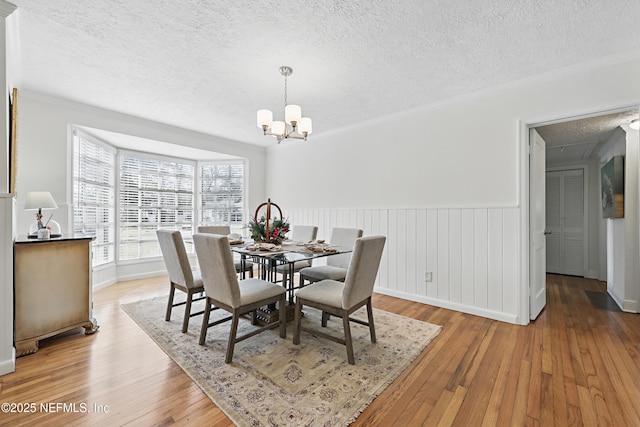 dining room featuring a textured ceiling, light wood-style flooring, a wainscoted wall, ornamental molding, and an inviting chandelier