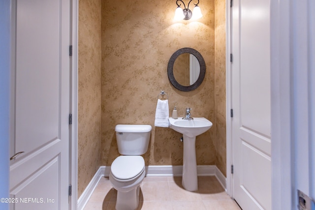 half bathroom with toilet, wallpapered walls, tile patterned flooring, and baseboards