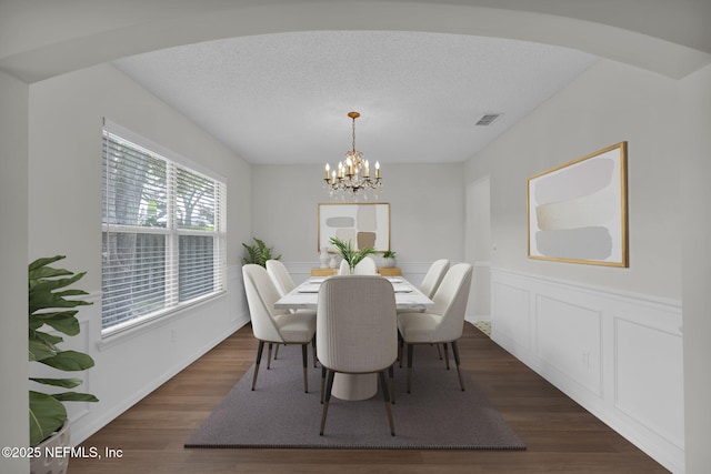 dining space with dark wood-style floors, a wainscoted wall, visible vents, an inviting chandelier, and a textured ceiling