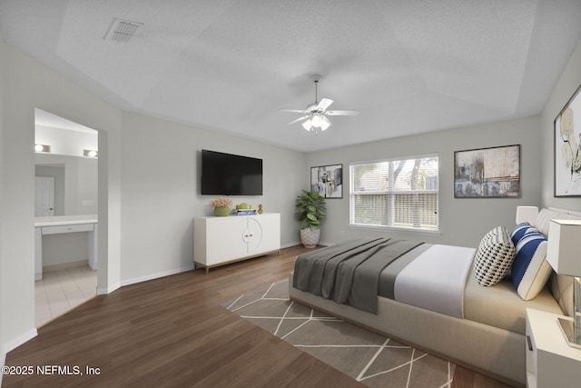 bedroom featuring dark wood-style floors, visible vents, a textured ceiling, and ensuite bathroom