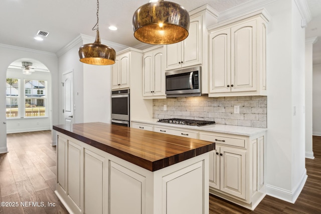 kitchen with butcher block countertops, appliances with stainless steel finishes, dark wood-type flooring, crown molding, and backsplash