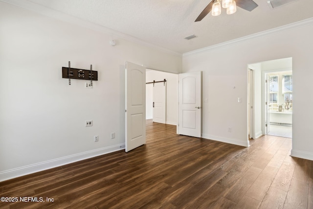 unfurnished bedroom featuring dark wood-type flooring, visible vents, crown molding, and a barn door