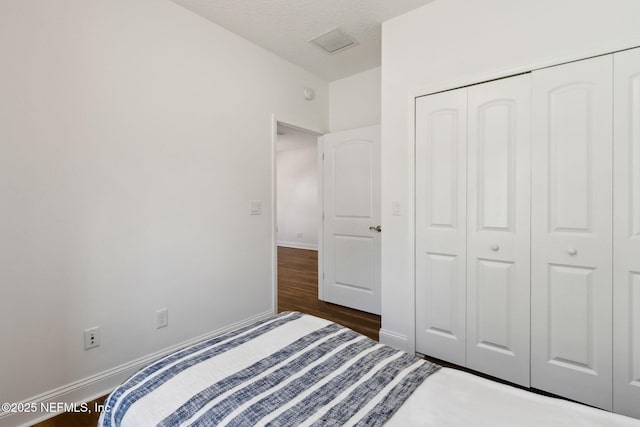 unfurnished bedroom featuring a textured ceiling, dark wood-style flooring, visible vents, baseboards, and a closet