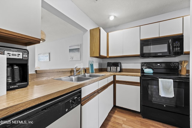 kitchen with light wood finished floors, a sink, black appliances, a textured ceiling, and white cabinetry