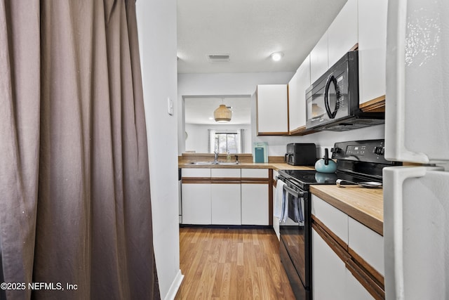 kitchen with white cabinetry, black appliances, visible vents, and wood counters