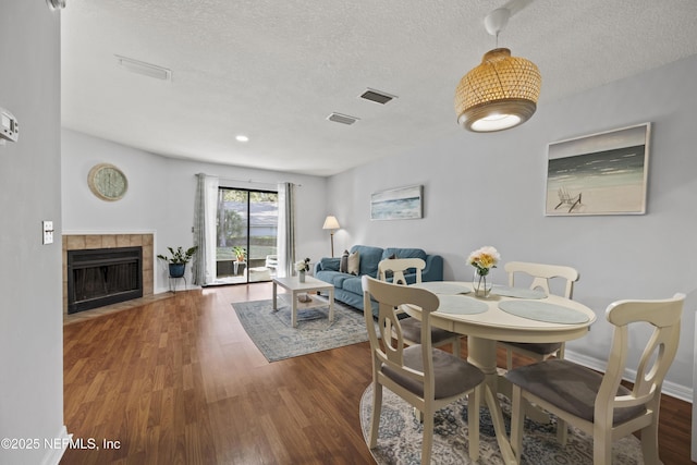 dining room with visible vents, a tile fireplace, a textured ceiling, and wood finished floors