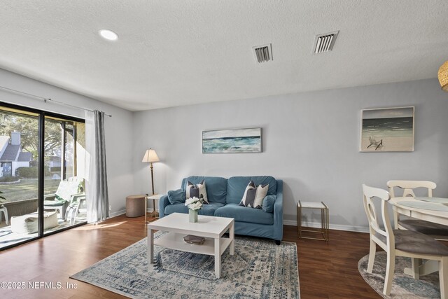 living area with a textured ceiling, wood finished floors, visible vents, and baseboards