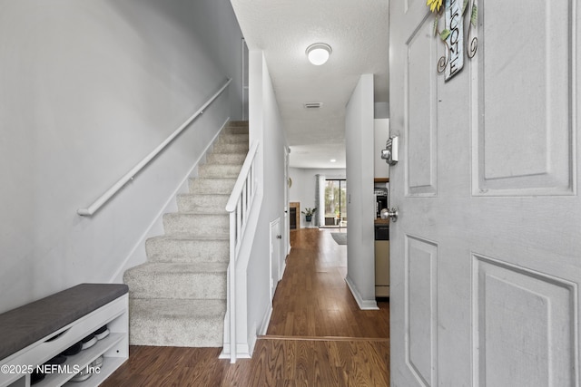 foyer entrance featuring baseboards, visible vents, dark wood finished floors, stairs, and a textured ceiling