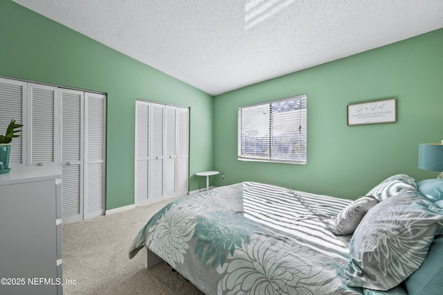 carpeted bedroom featuring baseboards, a textured ceiling, two closets, and lofted ceiling