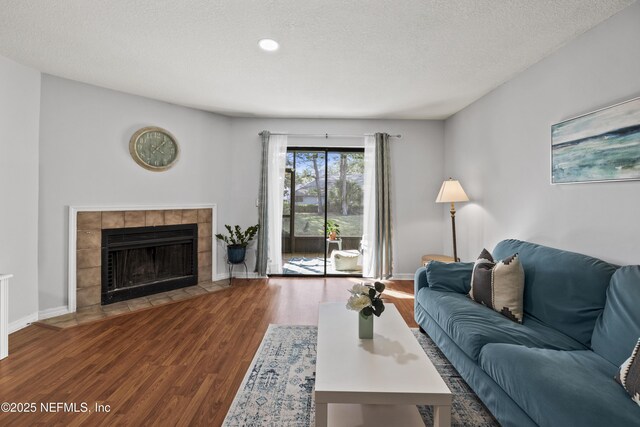 living room with baseboards, a textured ceiling, wood finished floors, and a tiled fireplace